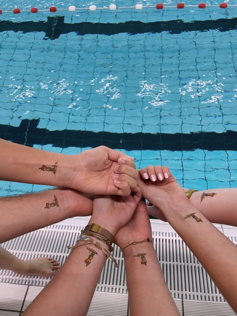 Zes polsen bij de rand van een zwembad, elk met dezelfde zelfontworpen tijdelijke tattoo