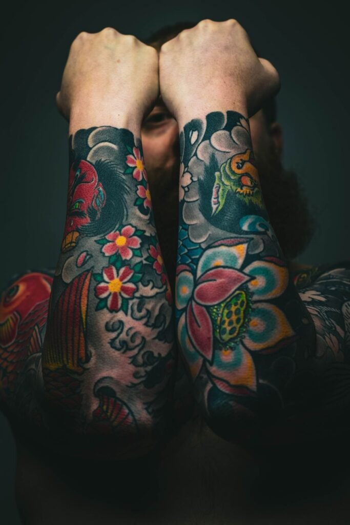 Twee onderarmen vol kleurrijke old school tattoos met bloemen en koivissen